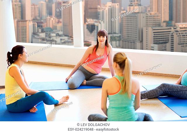 pregnancy, sport, fitness, people and healthy lifestyle concept - group of happy pregnant women sitting and talking on mats in gym