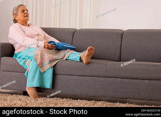 Old woman applying hot water bag for relieving from knee joint pain