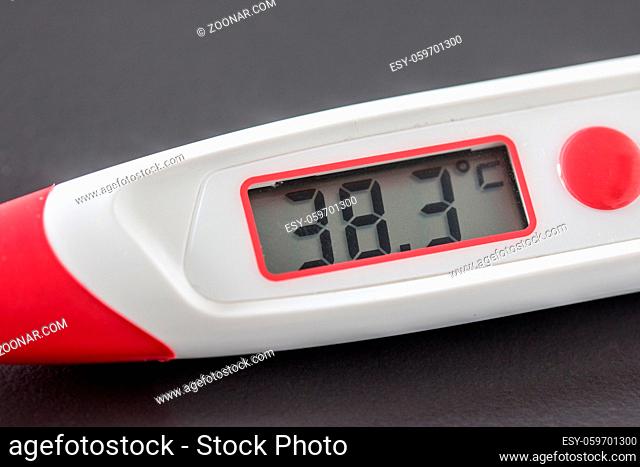 Red fever thermometer with digital display and 38 degrees Celsius lying on the desk