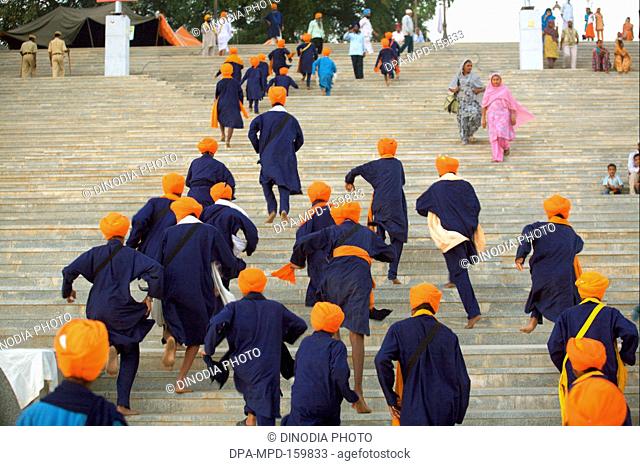 Group of young Sikh boys in blue clothes with saffron head-gear climbing stairs of Sachkhand Saheb Gurudwara ; 300th year of Consecration of  Guru-Granth Sahib...