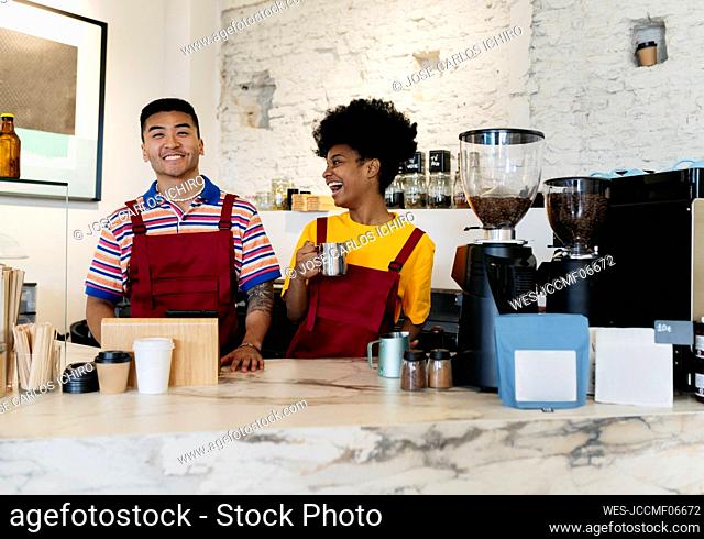 Cheerful woman holding coffee mug looking at colleague standing at checkout