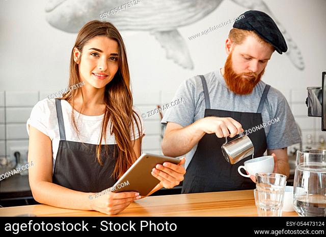 Coffee Business Concept - Cheerful baristas looking at their tablets for online orders in modern coffee shop