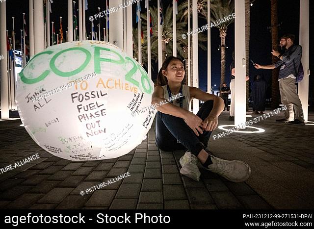 12 December 2023, United Arab Emirates, Dubai: A woman sits next to a globe labeled ""COP28"". The World Climate Conference has gone into extra time after a...