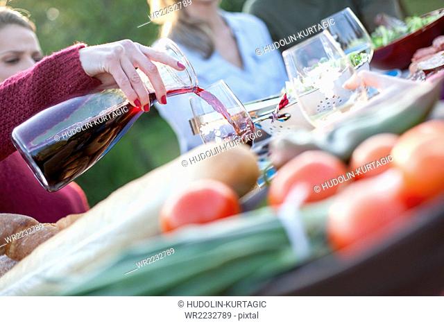Pouring red wine into glass on garden party