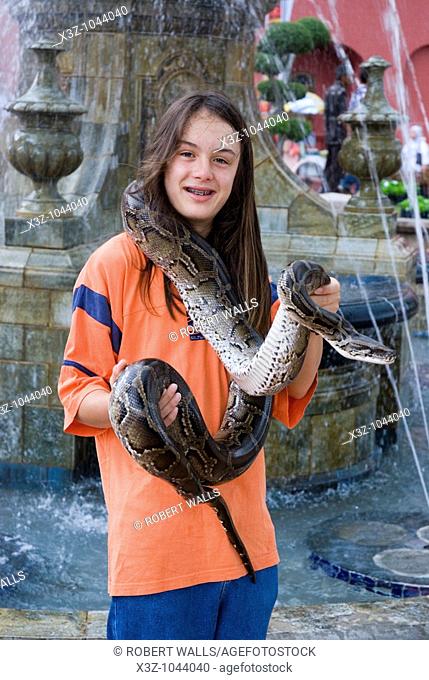 A long haired boy poses for s photo holding a python in Malacca Malaysia