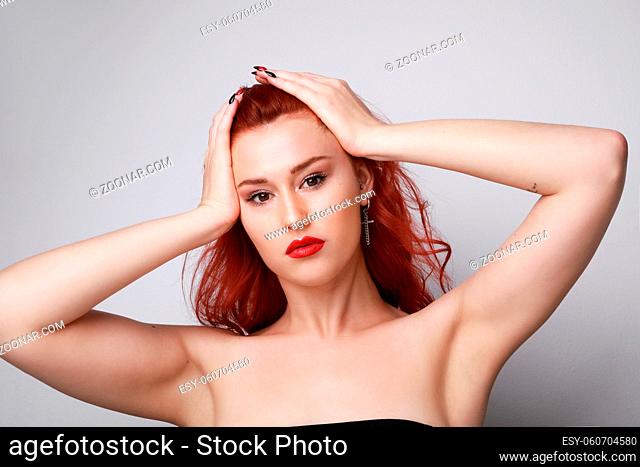 Close-up of young woman with red hair posing over grey background. High quality photo