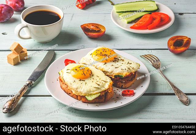 Breakfast toasts with vegetables and fried egg on white plate, cup of coffee and some fruits over wooden background. Clean eating food concept