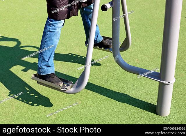 An elderly woman trains her legs on a public sports simulator. Sunny spring April day. Natural colors simplistic image