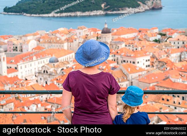 Caucasian Mother and daughter tourists wearnig blue hats standing on top of Old Town Walls in Dubrovnik admiring the view of the historical city below, Croatia