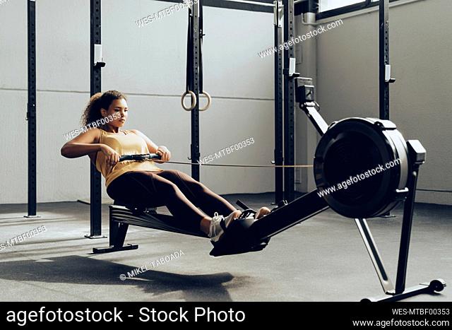 Young woman exercising in gym with rowing machine