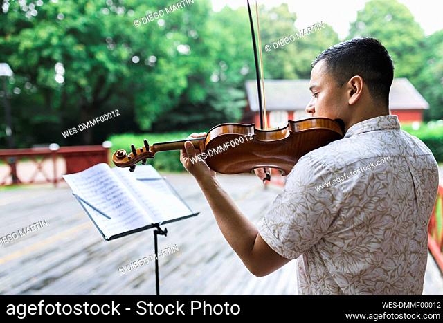Young violinist playing violin by sheet music at park
