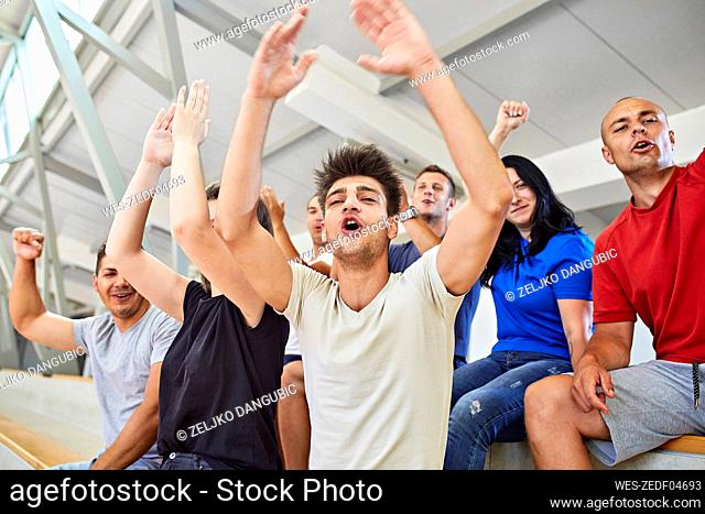 Man with arms raised cheering with friends in stadium