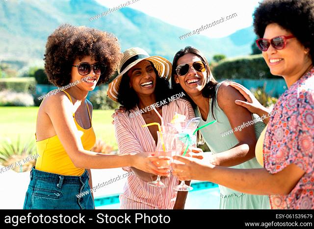 Happy biracial young female friends toasting cocktails while having fun at pool party in summer