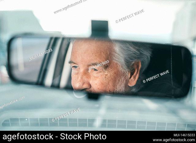 Portrait of one old pensioner man driving and enjoying his new car. Rear view mirror