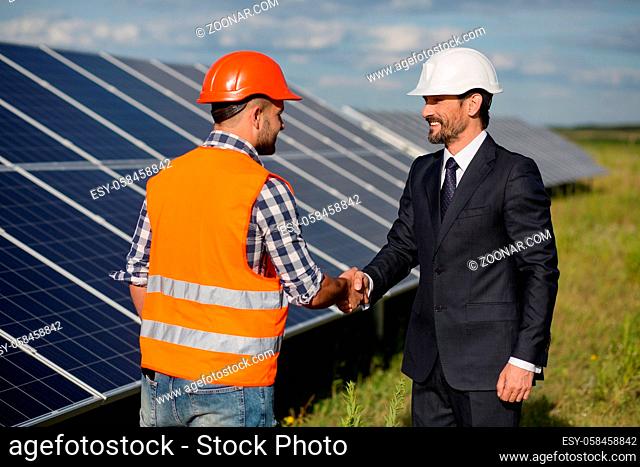 Businessman and foreman shaking hands at solar energy station. Solar panels in the field, two men making agreement