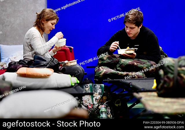 04 March 2022, Hungary, Zahony: A woman and a young man who fled Ukraine sit on cots and eat in a school gymnasium converted into an emergency shelter in Zahony...