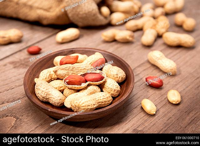 Peanuts in bowl on rustic wooden table. Arachis hypogaea