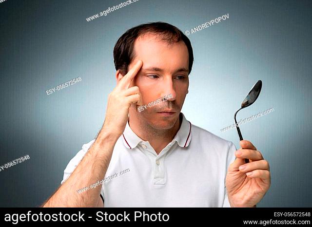 Portrait Of A Man Using Telekinetic Powers Holding Stainless Steel Spoon Against Gray Background