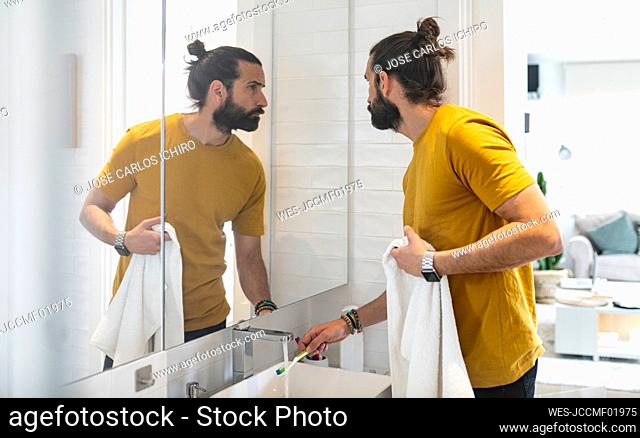 Handsome man washing toothbrush while looking in mirror at home