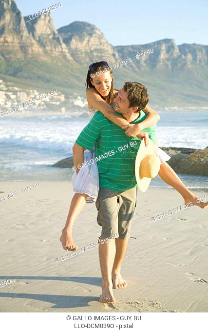 Man giving his partner a piggy back ride on the beach with Table Mountain in the background, Cape Town, Western Cape Province, South Africa