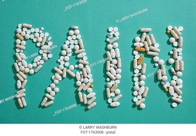 Painkiller pills spelling out Pain on green background