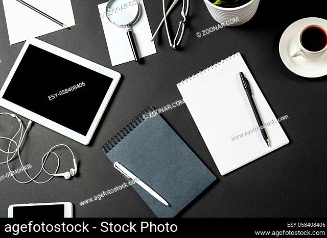 Top view of modern workplace with tablet computer. Flat lay composition with cup of coffee and office supplies on black surface