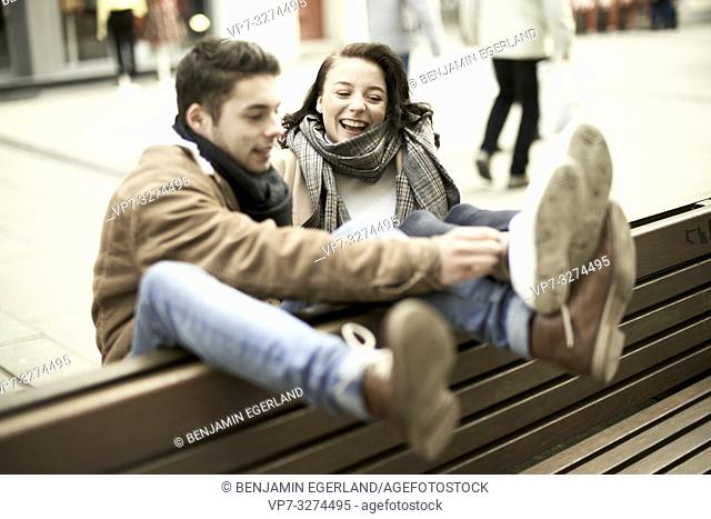 young teenage couple sitting on bench the wrong way round in city, hanging out together, legs up, upside down, in Cottbus, Brandenburg, Germany