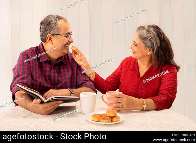 A HAPPY WIFE CHEERFULLY GIVES A CUPCAKE TO HER HUSBAND