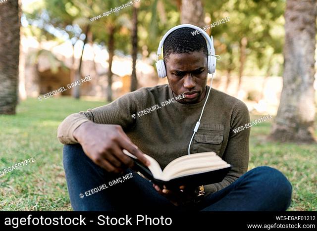 Male entrepreneur reading book while sitting on grass in park