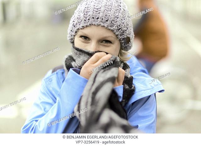 woman wrapping scarf around face, outdoors in city in bad weather, in Munich, Germany