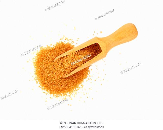 Close up one wooden scoop spoon full of raw brown cane sugar with pinch spilled and spread around, isolated on white background, elevated top view