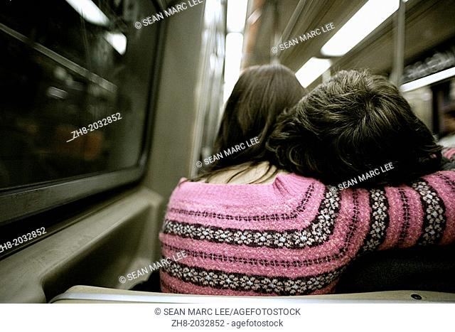 A woman in a pink sweater cradles a man's head on her shoulder while on a subway train in New York