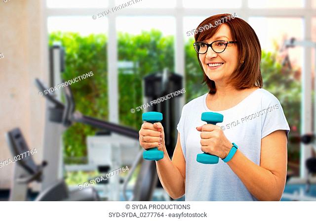 happy old woman with dumbbells exercising in gym