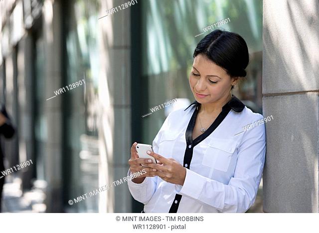 Business people outdoors, keeping in touch while on the go. A woman in a white jacket checking her phone