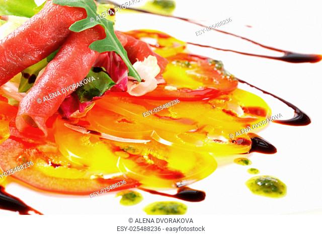 Thinly sliced bell peppers and raw beef garnished with pesto and balsamic vinegar