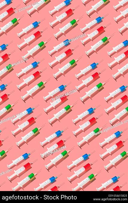 Vertical medical pattern from surgical disposable syringes with red, green and blue serum or drugs for injections on a living coral background, hard shadows