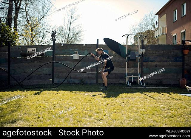 Man exercising with battle ropes in garden