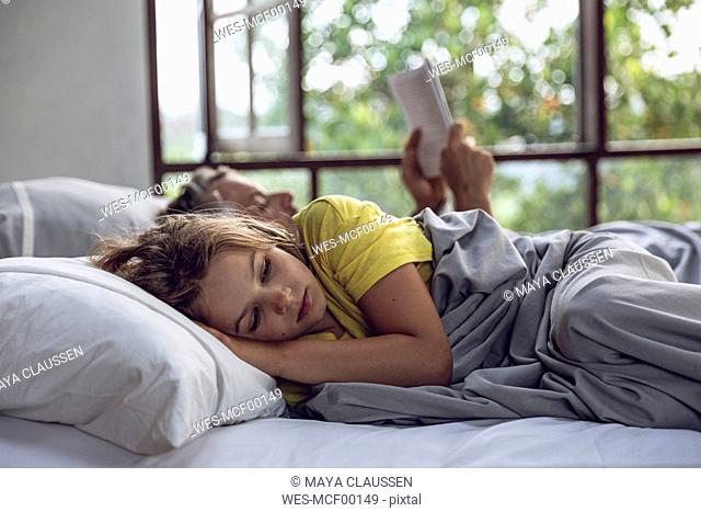 Girl lying in bed with father reading book