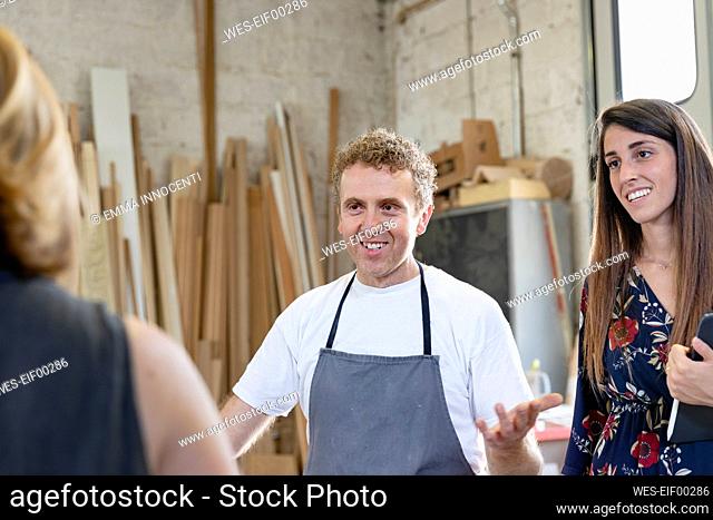 Smiling coworker and project manager talking to employee while standing at workshop