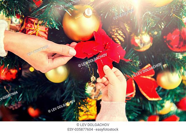 family, christmas, holidays, new year and people concept - close up of mother and child hands decorating christmas tree