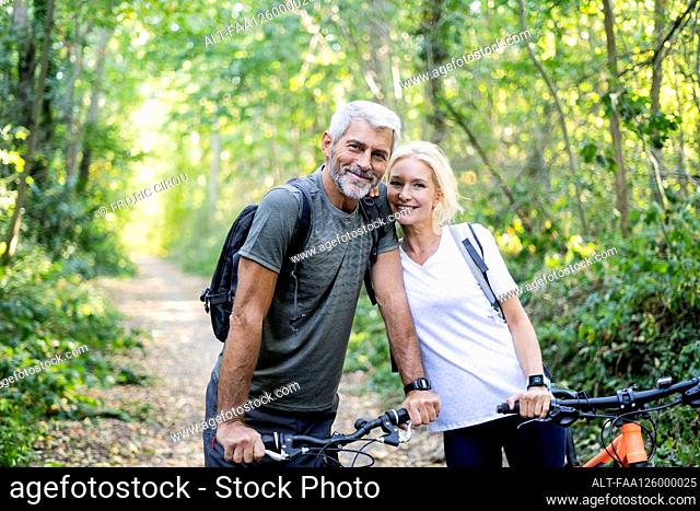 Portrait of smiling mature couple with bicycles standing in forest