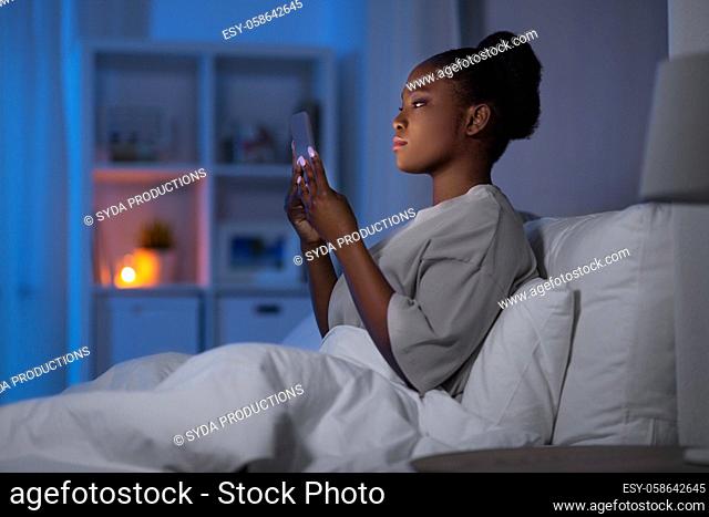 woman with smartphone in bed at home at night