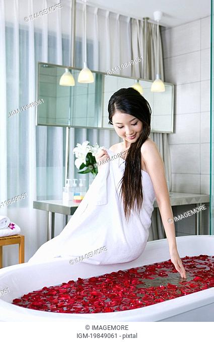 Young woman wearing a towel and looking at roseleaves in the bathtub