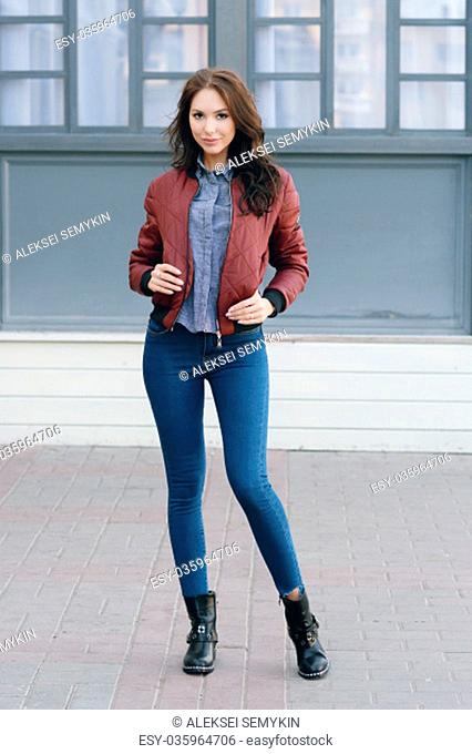 Young beautiful stylish woman in a burgundy pilot's jacket and blue jeans, street style, spring and autumn trend, look, hair in the wind