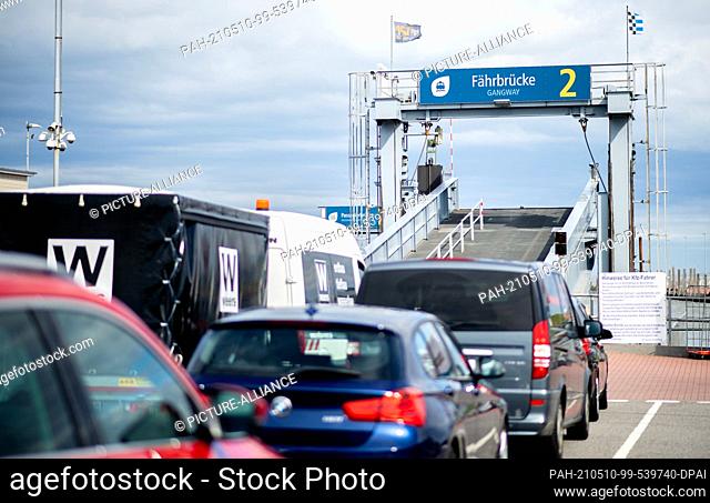 10 May 2021, Lower Saxony, Norddeich: Tourists stand with their cars at the ferry dock in front of a ferry bridge and wait for the departure to the island of...