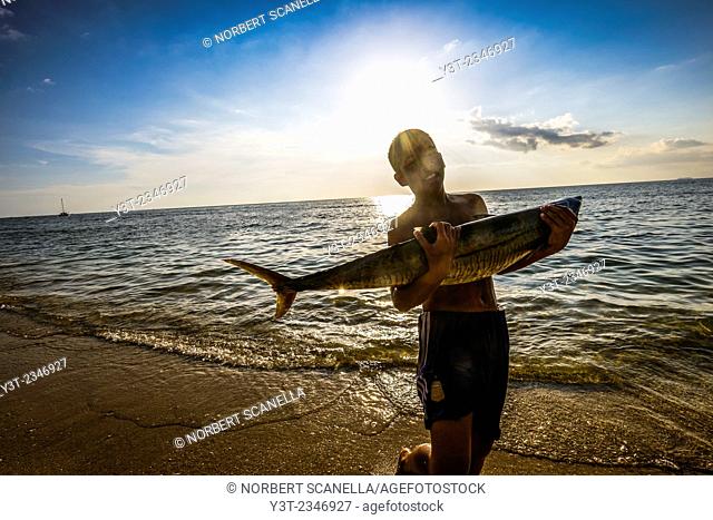 Asia. Thailand. Andaman Sea. Koh Lanta island. Klong Khong Beach. Back from fishing. Young boy carrying Barracuda