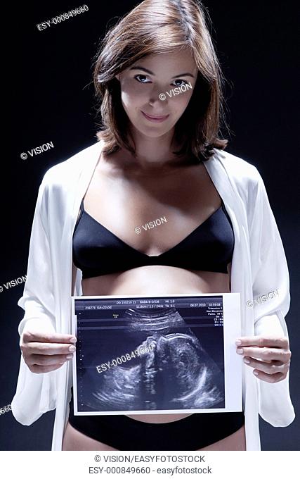 smiling caucasian pregnant holding ultrasound scan woman portraitt in nightie on studio isolated black background