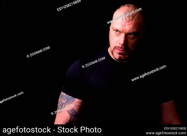 Studio shot of muscular bald bearded man looking macho against black background