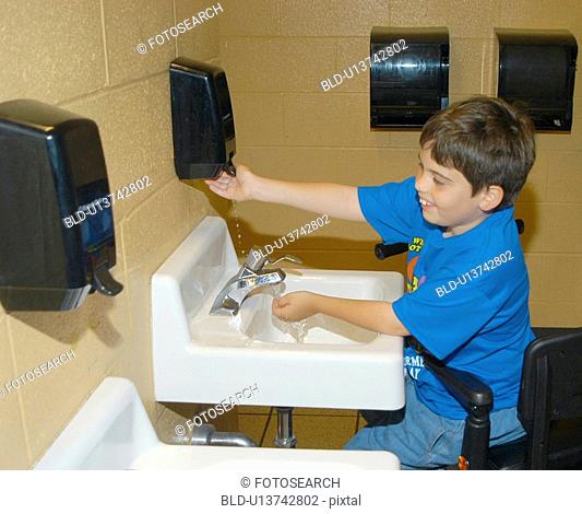 Boy with Muscular Dystrophy, utilizing a scooter/cart for mobility, washing his hands in the restroom