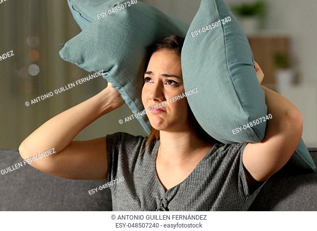 Annoyed woman suffering neighbour noise sitting on a couch in the living room at home